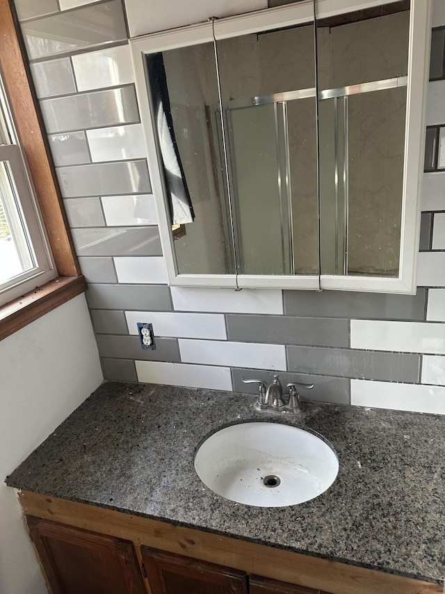 bathroom with a shower with shower door, vanity, and decorative backsplash