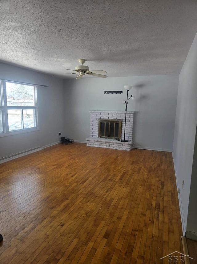 unfurnished living room featuring a ceiling fan, hardwood / wood-style flooring, baseboard heating, a textured ceiling, and a fireplace