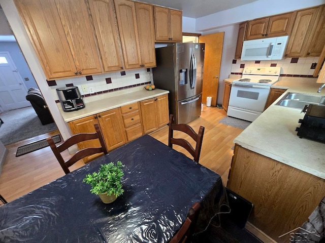 kitchen featuring tasteful backsplash, light countertops, light wood-style floors, a sink, and white appliances