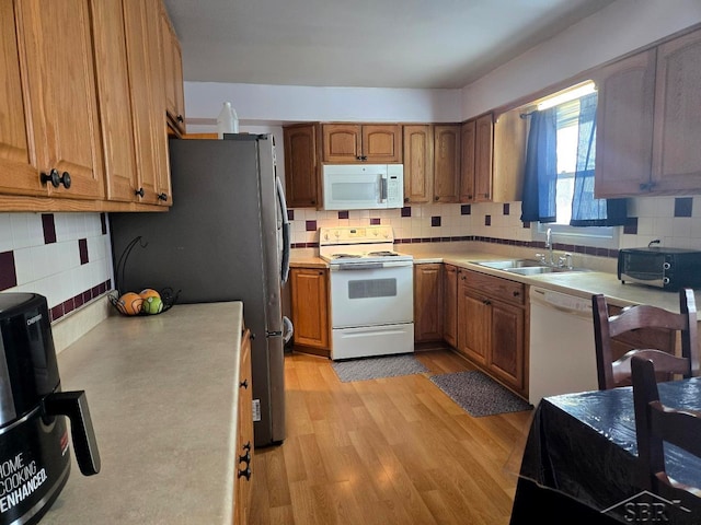 kitchen featuring white appliances, tasteful backsplash, light countertops, light wood-type flooring, and a sink