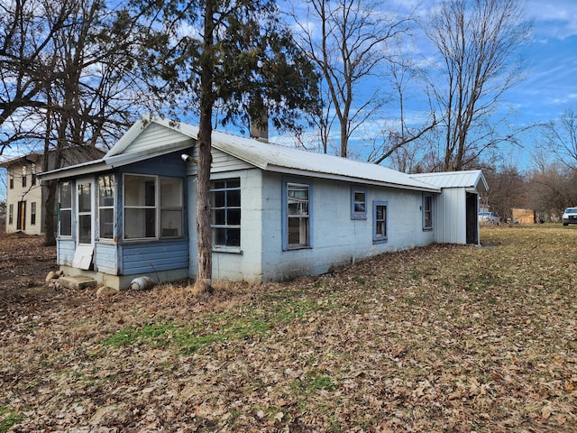 view of side of home with a sunroom, concrete block siding, and metal roof