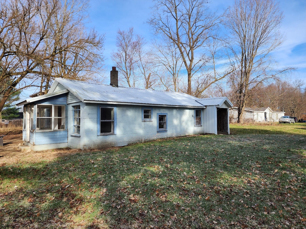 rear view of property featuring a chimney, metal roof, concrete block siding, and a lawn