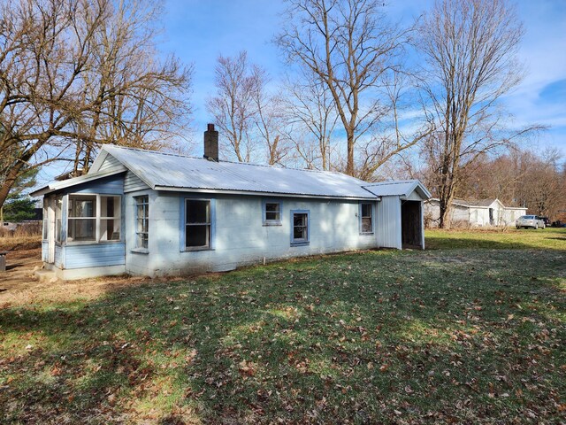 rear view of property featuring a chimney, metal roof, concrete block siding, and a lawn
