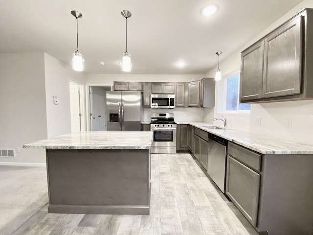 kitchen featuring stainless steel appliances, visible vents, hanging light fixtures, a sink, and a kitchen island