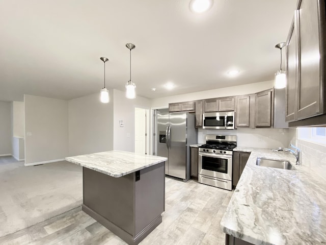 kitchen with light stone counters, a center island, stainless steel appliances, hanging light fixtures, and a sink