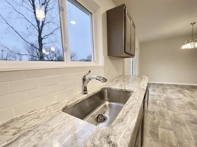 kitchen featuring light stone counters, decorative light fixtures, a notable chandelier, tasteful backsplash, and a sink