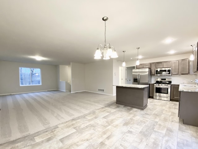 kitchen with visible vents, appliances with stainless steel finishes, a center island, an inviting chandelier, and a sink