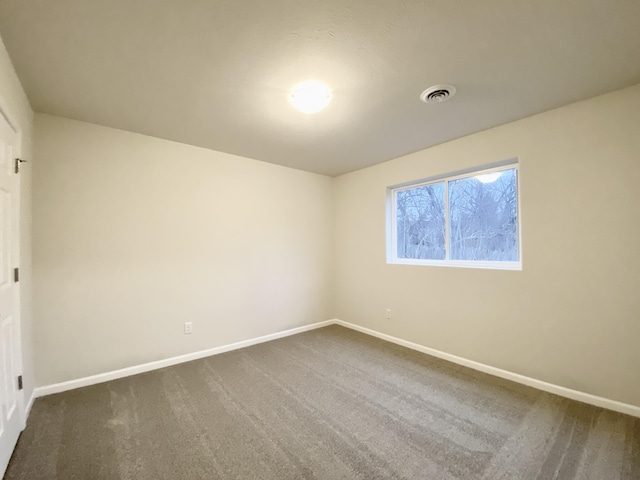 spare room with dark carpet, visible vents, and baseboards