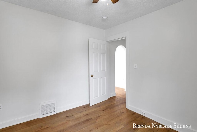 empty room featuring arched walkways, hardwood / wood-style floors, visible vents, and baseboards