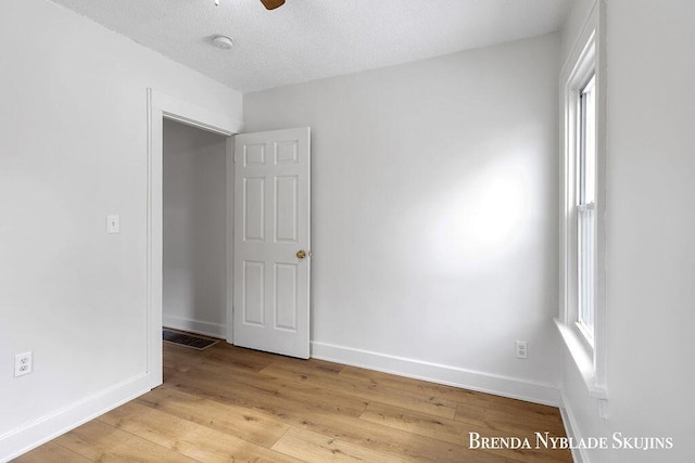 empty room with visible vents, a ceiling fan, a textured ceiling, light wood-type flooring, and baseboards