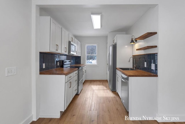 kitchen with a sink, appliances with stainless steel finishes, butcher block counters, and white cabinetry