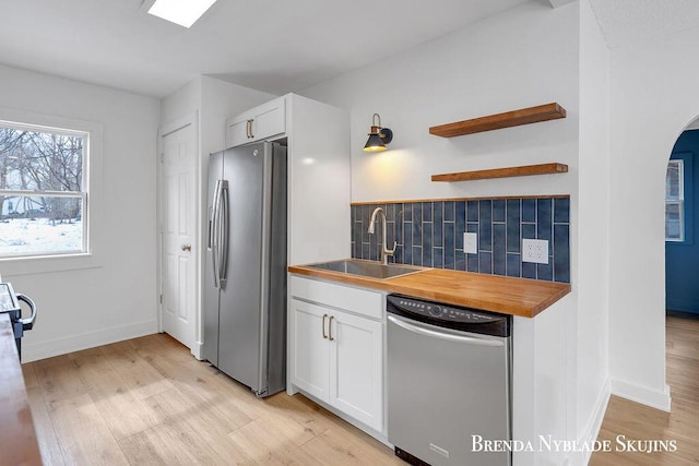 kitchen with arched walkways, a sink, stainless steel appliances, wooden counters, and backsplash