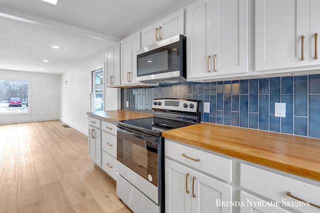 kitchen featuring range with electric stovetop, stainless steel microwave, backsplash, a healthy amount of sunlight, and butcher block countertops