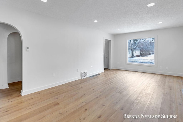 unfurnished room featuring arched walkways, recessed lighting, visible vents, light wood-style flooring, and a textured ceiling