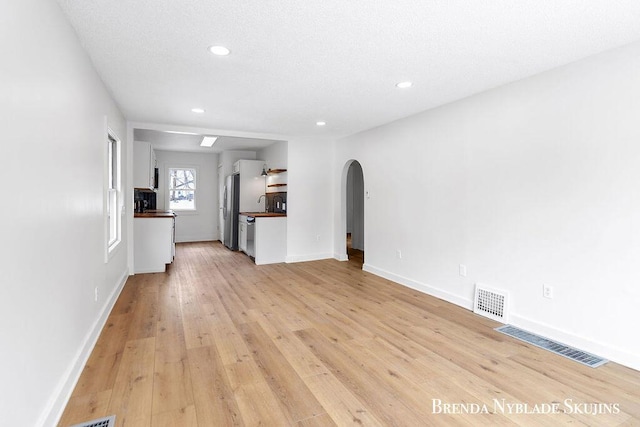 unfurnished living room with arched walkways, visible vents, light wood-style flooring, and baseboards