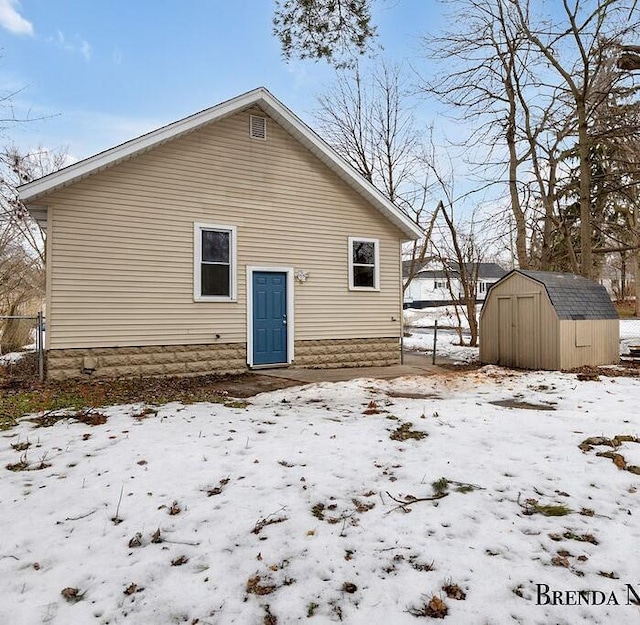 snow covered rear of property featuring a storage shed, an outdoor structure, and fence