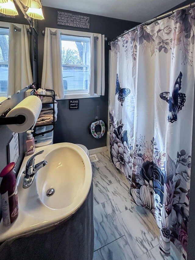 bathroom with curtained shower, marble finish floor, and a sink