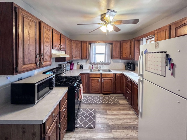 kitchen with under cabinet range hood, a sink, freestanding refrigerator, stainless steel microwave, and gas stove