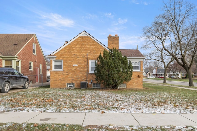 view of side of property with a chimney, central AC, and brick siding