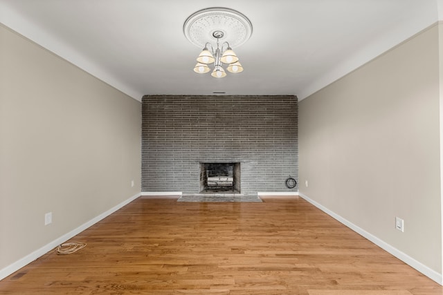 unfurnished living room featuring a brick fireplace, a notable chandelier, baseboards, and light wood-style floors