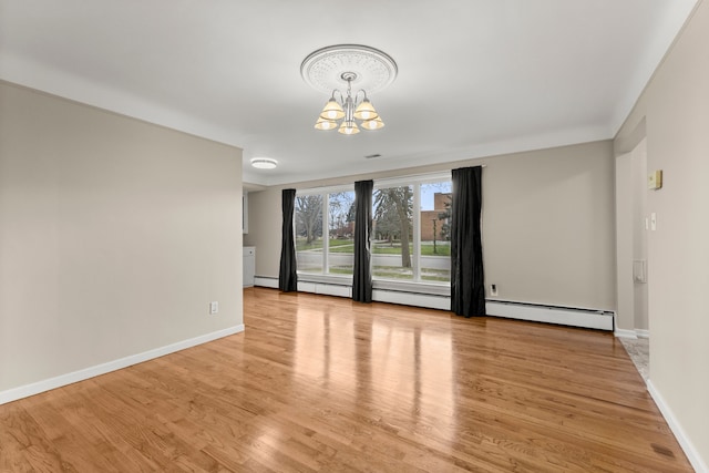 spare room featuring light wood-style floors, a baseboard radiator, baseboards, and a notable chandelier