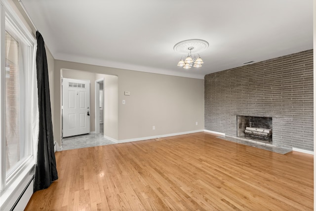 unfurnished living room featuring a notable chandelier, baseboards, light wood-style floors, baseboard heating, and a brick fireplace