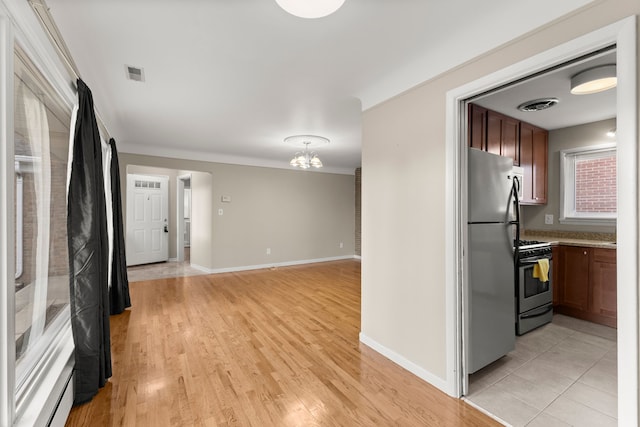 kitchen with visible vents, freestanding refrigerator, gas range, light wood-type flooring, and baseboards