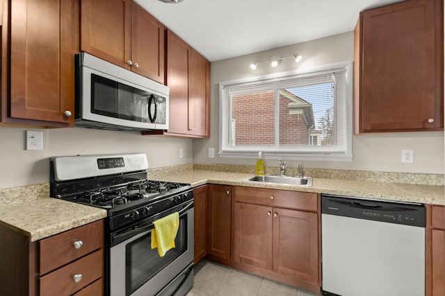 kitchen featuring light tile patterned floors, brown cabinetry, appliances with stainless steel finishes, light countertops, and a sink