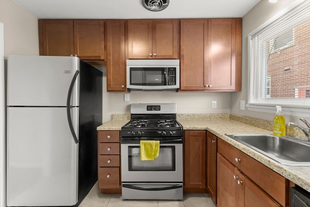 kitchen featuring stainless steel appliances, a sink, visible vents, light countertops, and brown cabinetry