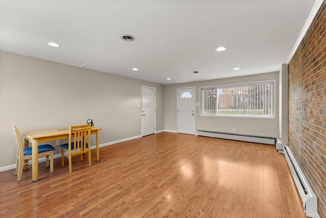 interior space featuring a baseboard radiator, visible vents, light wood-style flooring, a baseboard heating unit, and brick wall