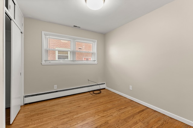 unfurnished bedroom with visible vents, baseboard heating, and light wood-style flooring