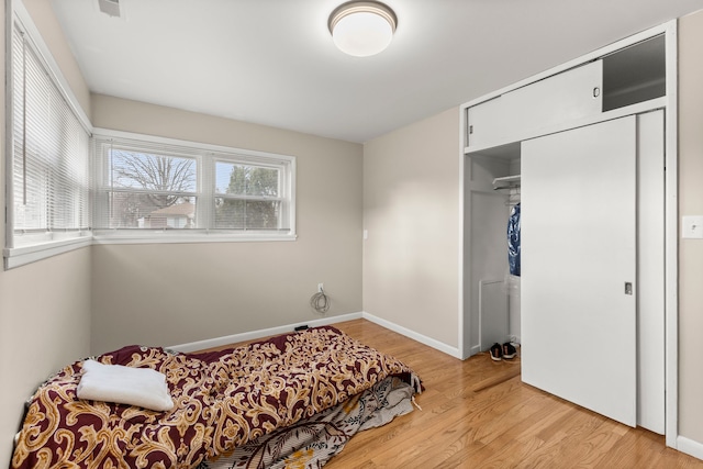 bedroom with light wood-type flooring, baseboards, and a closet