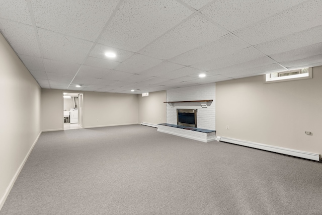 below grade area with a drop ceiling, a baseboard heating unit, baseboards, a brick fireplace, and carpet