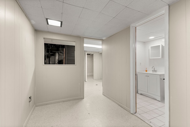 hallway with light floors, baseboards, a drop ceiling, and a sink