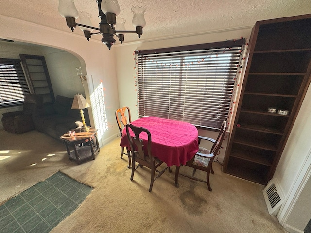 carpeted dining space featuring arched walkways, a healthy amount of sunlight, a textured ceiling, and an inviting chandelier