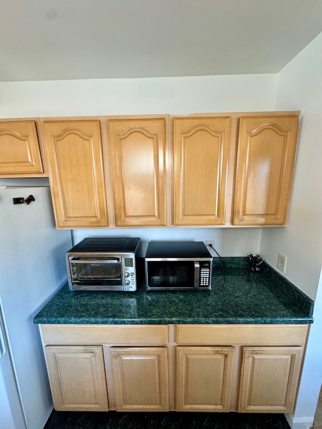 kitchen with dark countertops, freestanding refrigerator, stainless steel microwave, and light brown cabinetry