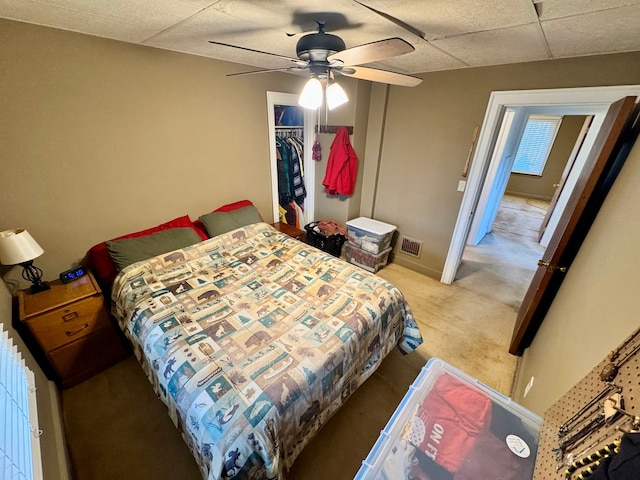 bedroom with a closet, visible vents, light carpet, ceiling fan, and a drop ceiling