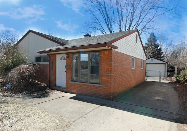 ranch-style house featuring an outbuilding, brick siding, a shingled roof, a detached garage, and concrete driveway