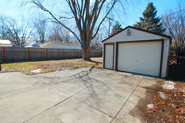 detached garage featuring concrete driveway and fence