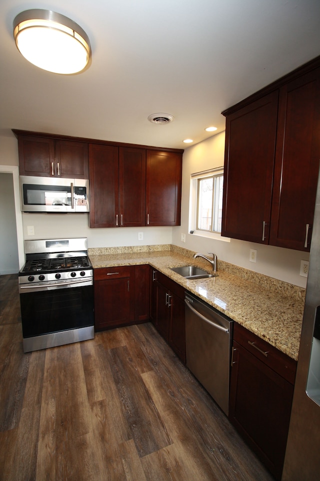 kitchen featuring visible vents, appliances with stainless steel finishes, dark wood-style flooring, light stone countertops, and a sink