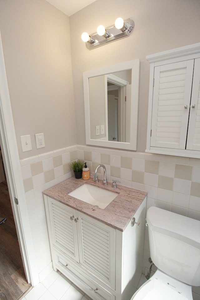 half bath featuring a wainscoted wall, tile walls, toilet, vanity, and tile patterned flooring