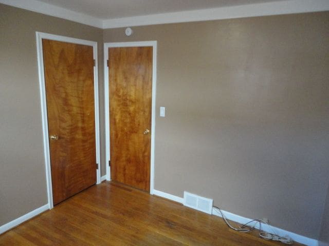 unfurnished room featuring baseboards, visible vents, and wood finished floors