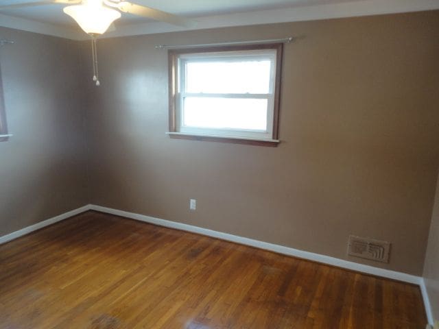 spare room with a ceiling fan, visible vents, baseboards, and wood finished floors