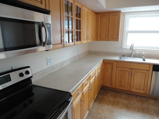 kitchen with light tile patterned floors, a sink, light countertops, appliances with stainless steel finishes, and glass insert cabinets