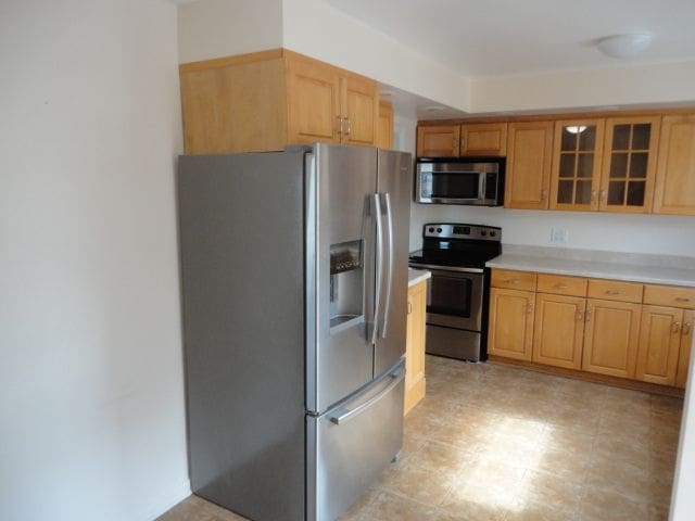 kitchen with stainless steel appliances, light countertops, and glass insert cabinets