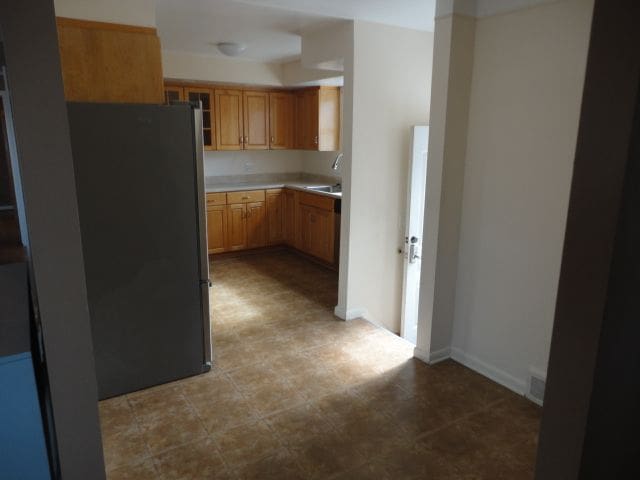 kitchen with a sink, visible vents, baseboards, light countertops, and freestanding refrigerator