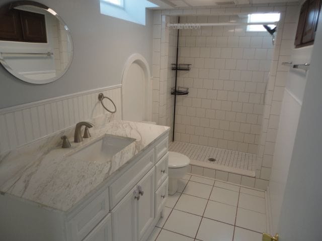 bathroom featuring toilet, a wainscoted wall, tile patterned flooring, a tile shower, and vanity