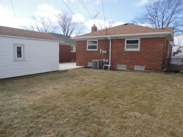 back of house featuring a patio, central air condition unit, brick siding, a lawn, and a chimney