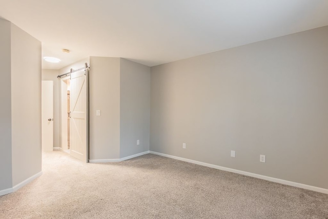 spare room with light carpet, baseboards, and a barn door