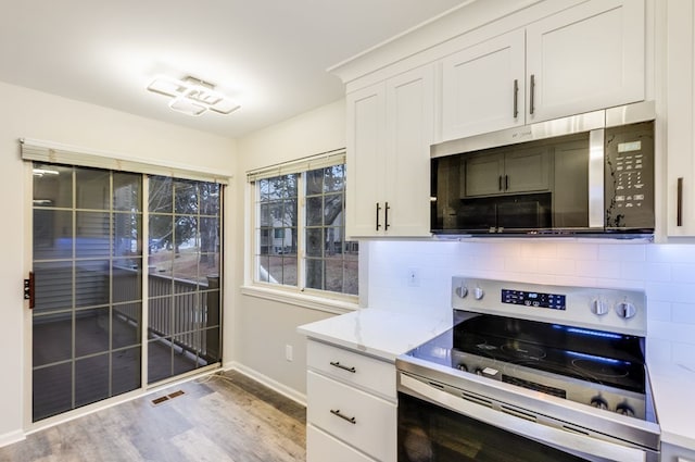 kitchen with light stone counters, stainless steel appliances, visible vents, light wood finished floors, and tasteful backsplash